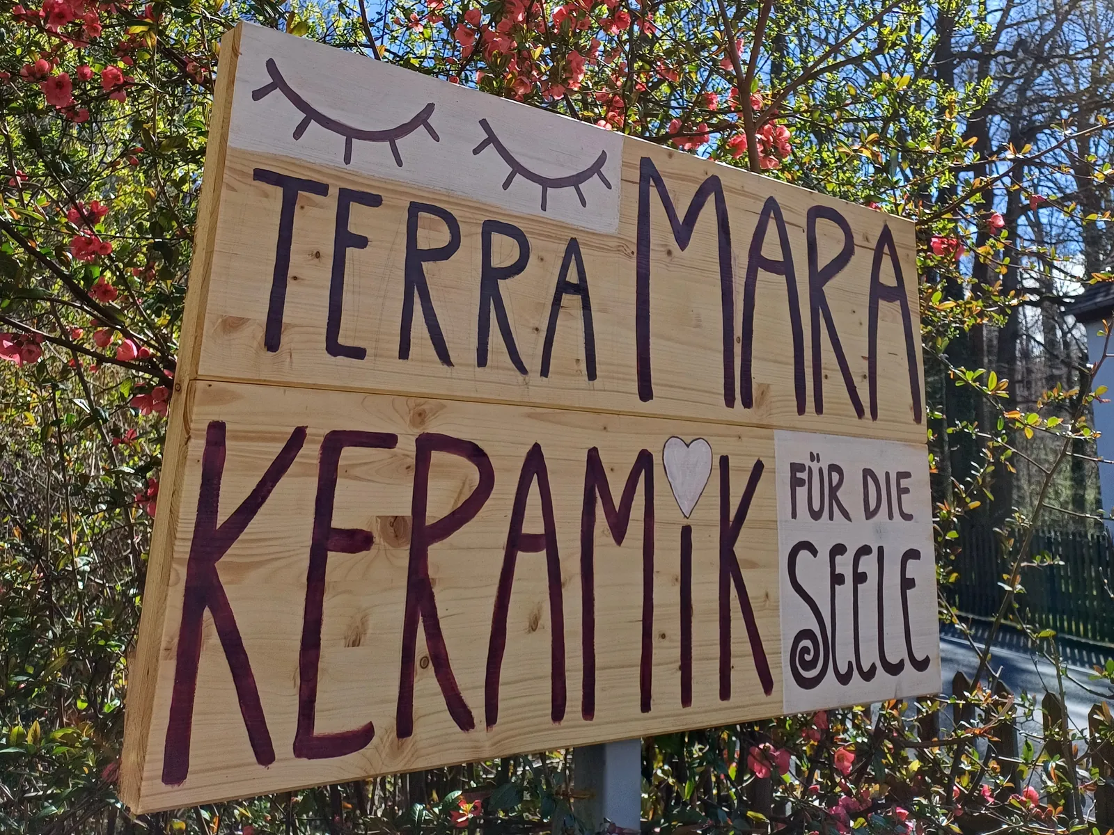 Handbemaltes Holzschild „TERRA MARA – Keramik für die Seele“ zwischen blühenden Sträuchern