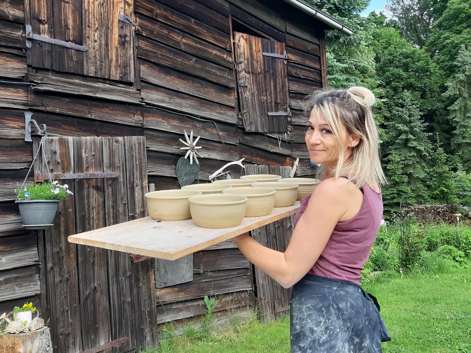 Mareike trägt ein Brett mit frisch gedrehten Schüsseln an der alten Holzscheune in Streitwald vorbei